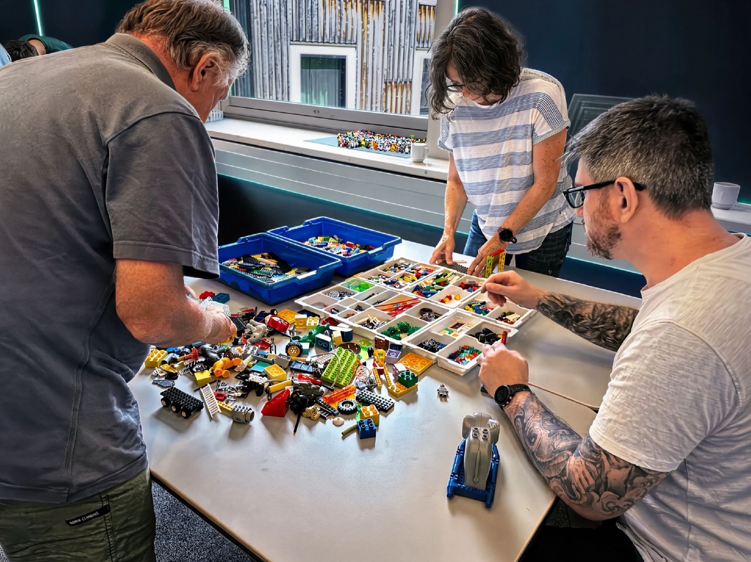 LEGO®-Serious-Play-Workshop: Teilnehmer wählen Steine aus Sortierkästen auf einem großen Arbeitstisch (Farbbearbeitung)
